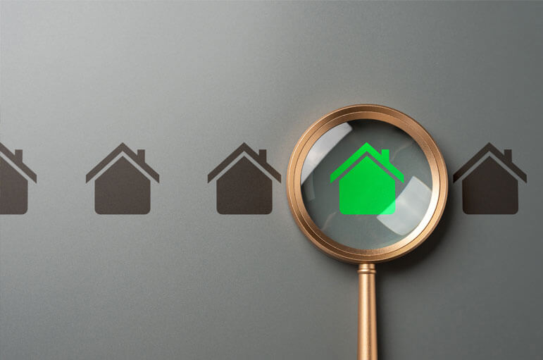 A magnifying glass hovers over several tiny little homes and identifies a green one.